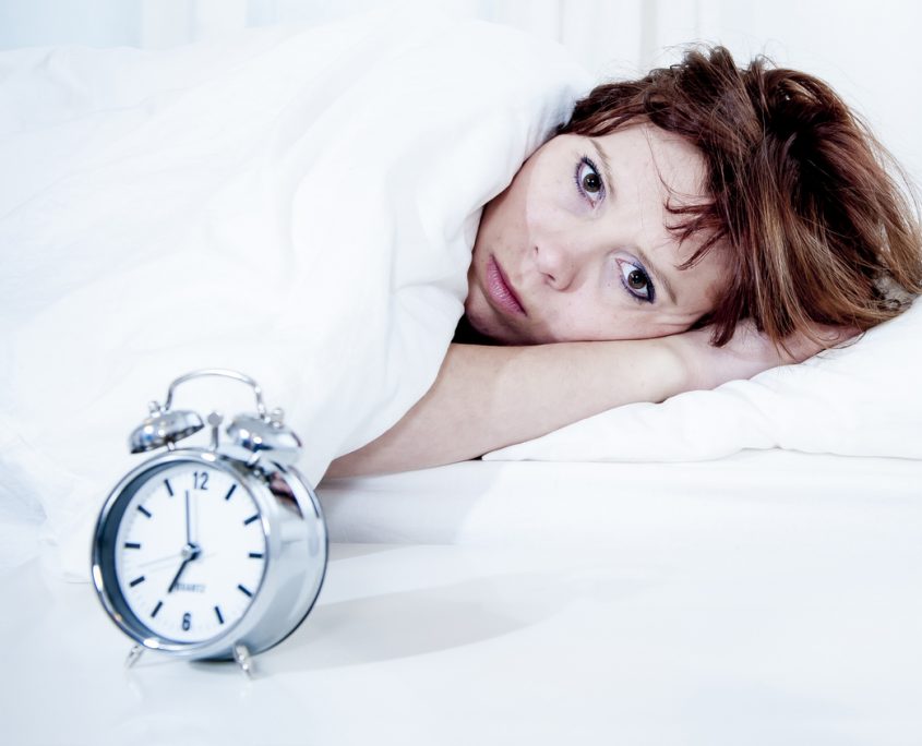 woman with red hair in her bed with insomnia and can't sleep waiting for her alarm clock to go off on a white background