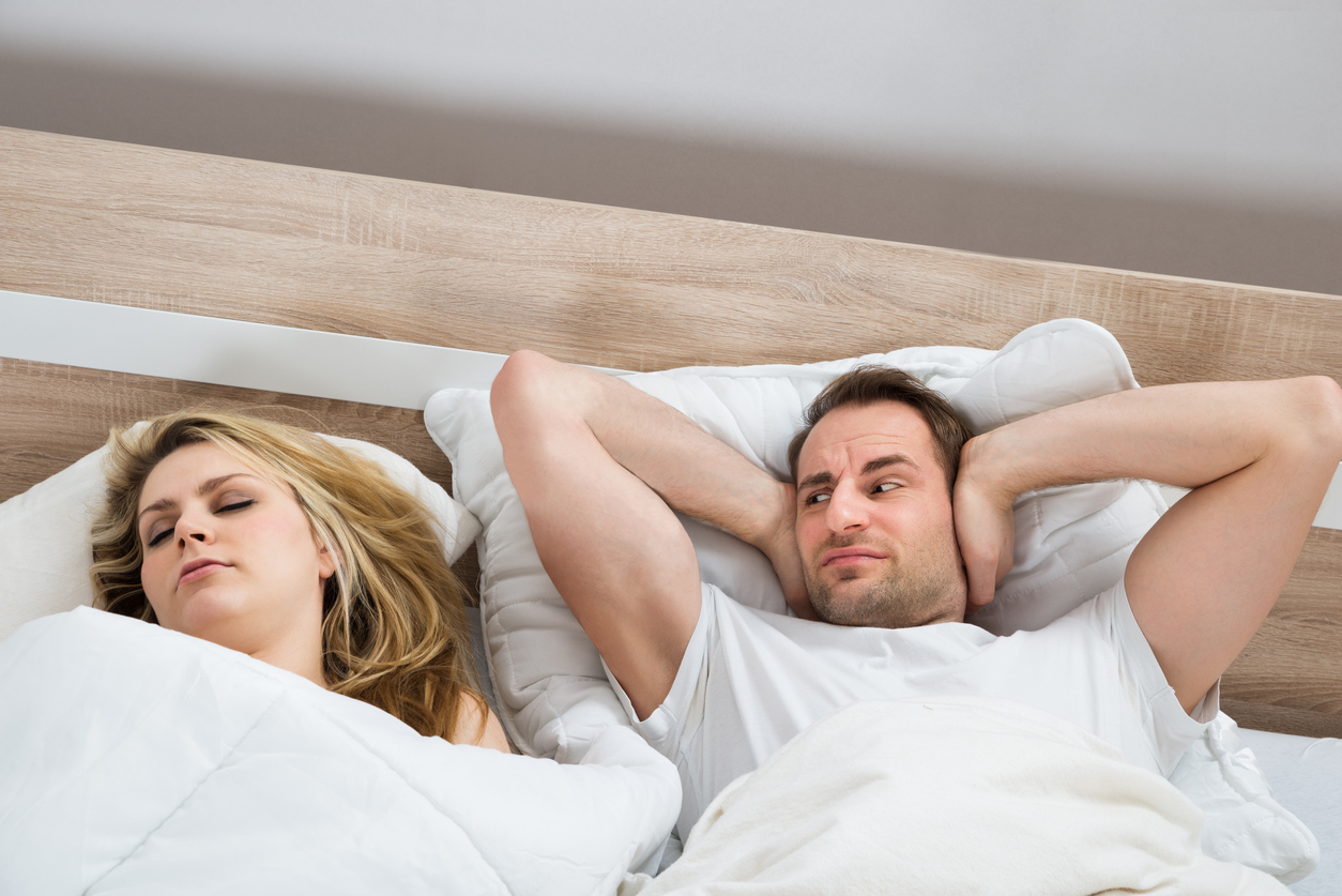 Man Covering Ears While Woman Sleeping In Bedroom At Home
