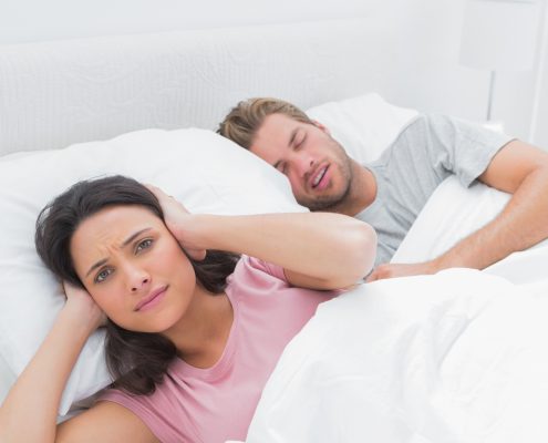 Annoyed woman covering her ears while her husband is snoring